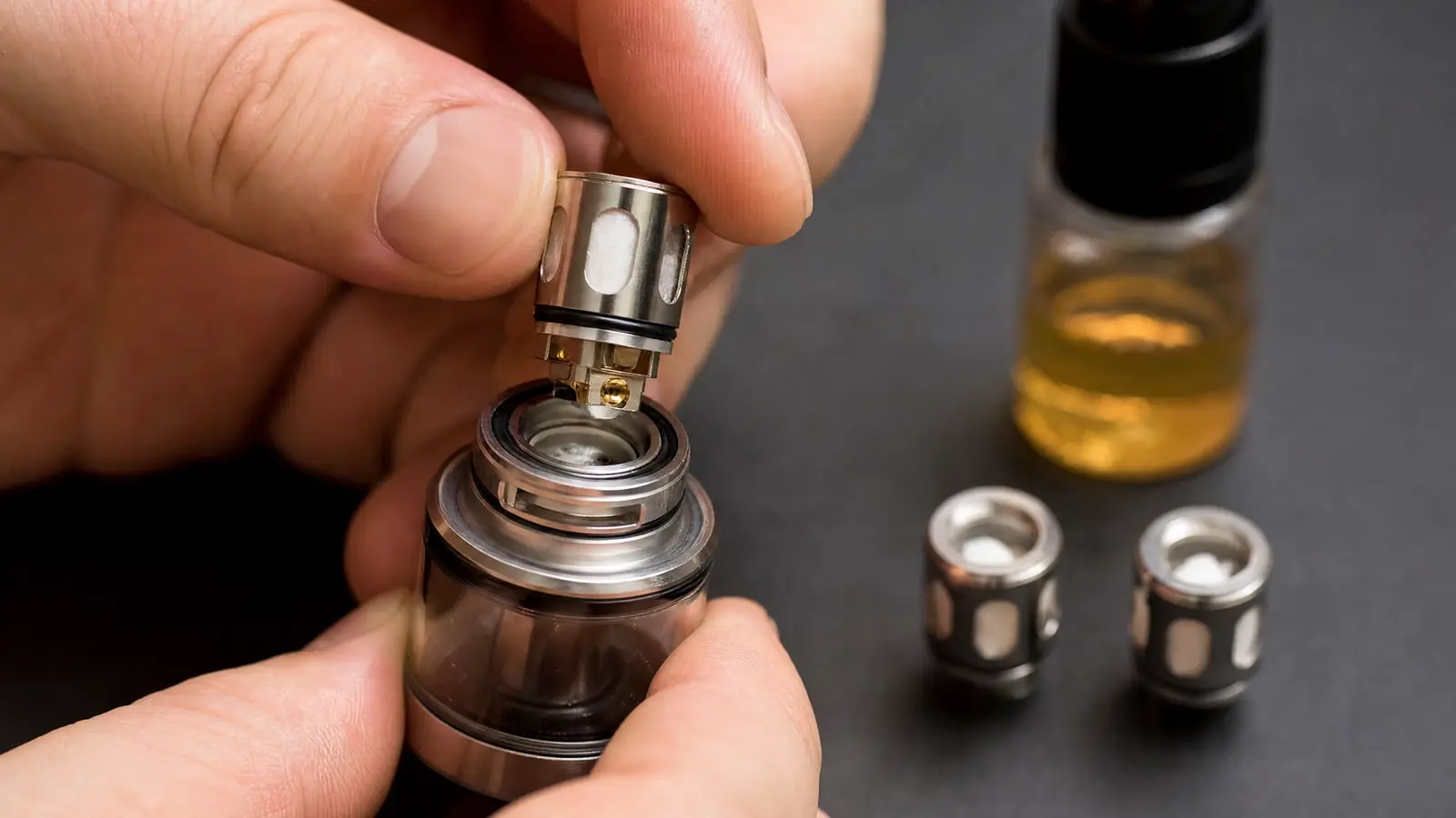 Hand wechselt den Verdampferkopf an einem Pod-Tank, daneben neue Coils